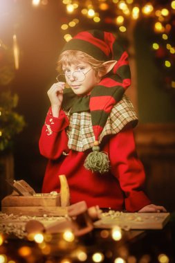 Küçük şirin elf çocuk Noel 'de marangozluk atölyesinde çocuklar için tahta oyuncaklar yapıyor. Noel Baba atölyesi. Sihirli ışıklar yanıp sönüyor. Noel Masalı.