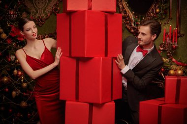 Noel ve yeni yıl alışverişi. Zarif takım elbiseli neşeli bir adam ve güzel, zarif bir kız bir yığın hediyenin arkasından birbirlerine şakacı bir şekilde bakıyorlar. Lüks Noel iç mimarisi.