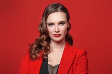 Zarif bir iş tarzı. Kırmızı arka planda parlak makyajlı güzel, kendine güvenen genç bir kadının portresi. Kadınlık, feminizm ve moda.