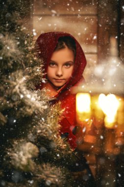 Eski bir peri masalının küçük kahramanı bir köknar ağacının yanında duruyor ve karlı bir Noel gecesinde yanan bir fener. Noel Masalı. Ahşap ev arka planı.