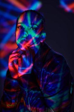 Sanal gerçeklik kavramı. Siyah deri ceketli, parlak makyajlı çekici bir esmer kızın portresi. Renkli lazer ışınlarıyla dolu karanlık bir yerde duruyor.. 