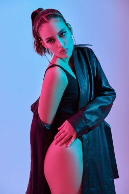 Çekici bir esmer kız modelinin stüdyo fotoğrafı. Siyah beden ve siyah deri ceketle karışık neon ışıkta poz veriyor. Moda fotoğrafı.. 