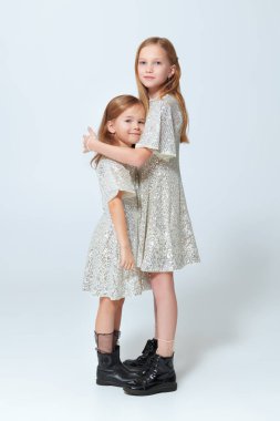 Beyaz arka planda poz veren parlak gümüş gece elbiseli iki güzel kızın tam boy portresi. Çocukların akşam modası. Noel ve Yeni Yıl Kutlaması.