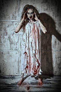 Saplantılı kadın. Soluk gözlü ve tüylü korkunç zombi kadın beton bir duvarın arkasında kanlı bir gecelik içinde duruyor. Korku, gerilim. Cadılar Bayramı. 