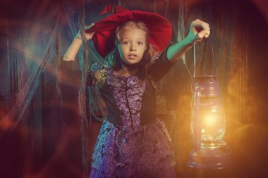 Cadı kostümü giymiş şirin bir kız çocuğu elinde fenerle karanlık eski bir kalede duruyor. Cadılar Bayramı süslemeleri. Cadılar Bayramı masalları.