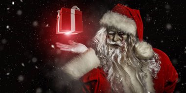 Noel ve Cadılar Bayramı. Korkunç Zombi Noel Baba elinde hediye kutusuyla şeytanca gülümsüyor. Parlayan yıldızlar ve kar yağışı olan siyah bir zemin. Boşluğu kopyala. 