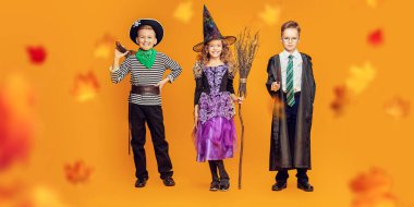 Cadılar Bayramı 'nda şeker mi şaka mı? Cadılar Bayramı kostümlü üç neşeli çocuk güz yapraklarıyla sarı bir arka planda neşeli poz veriyor. Stüdyo çekimi.