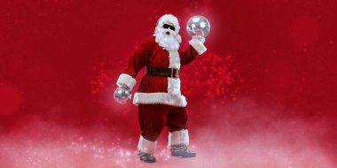 Havalı Noel Baba güneş gözlüğü takıyor kulaklıkla müzik dinliyor, disko toplarıyla şarkı söylüyor ve dans ediyor. Mutlu noeller. Parti zamanı. Sihirli ışıklarla süslü kırmızı arka plan. Boşluğu kopyala.