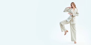 Beyaz bir stüdyo arka planında bol bej bir takım elbise giymiş güzel kahverengi saçlı bir mankenin tam boy çekimi. Zarif bir tarz. Moda fotoğrafı. Boşluğu kopyala.