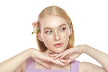 Hafif parlak makyajı, parlak çilleri ve soluk pembe gülleri olan narin sarışın bir kızın portresi. Güzellik konsepti. Kopyalama alanı olan beyaz arkaplan. Kozmetik ve makyaj malzemeleri. Güzellik ürünleri..