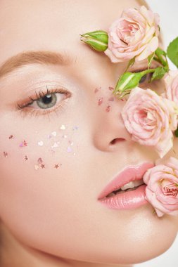 Güzellik konsepti. Açık renk makyajı, parlak çilleri ve soluk pembe gülleri olan narin sarışın bir kızın yakın plan portresi. Beyaz arka plan. Kozmetik ve makyaj malzemeleri. Güzellik ürünleri. Parfüm.