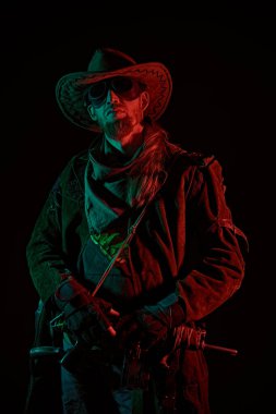 Deri ceketli, kovboy şapkalı ve gözlüklü, koyu bir arka planda duran, kırmızı ve yeşil ışıklı vahşi bir adam. Kıyameti haber veren kovboy.. 