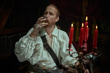 Beyaz gömlekli, geniş kollu yakışıklı bir asilzade kütüphanede oturmuş şarap içiyor. 16.-17. yüzyılın tarihi yeniden yapılandırması. 