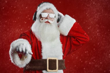 Modern disko Noel Baba 'nın portresi kulaklıklar ve karlı güneş gözlükleriyle. Karlı kırmızı stüdyo arka planı. Noel ve Yeni Yıl.