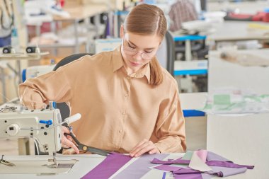Yaratıcı genç bir terzi kız atölyede yeni bir ürün dikiyor. Moda endüstrisi. Giysi imalatı.