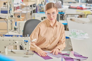 Dikiş atölyesi. Genç, güzel bir terzi dikiş makinesinde çalışıyor. Moda endüstrisi. Moda tasarımcısı.