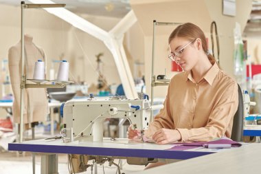 Güzel bir genç kızın dikiş atölyesinde yeni bir ürün dikerken çekilmiş fotoğrafı. Moda endüstrisi. Giysi imalatı.