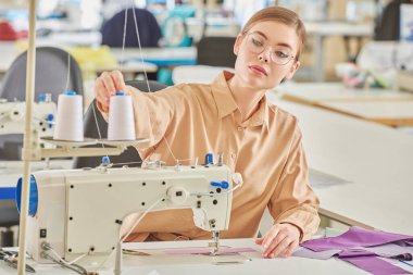 Güzel bir genç kız terzi dikiş atölyesinde yeni bir ürün dikiyor. Moda endüstrisi. Giysi imalatı.