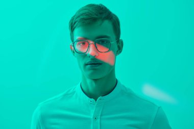 Zarif beyaz gömlekli ve şık gözlüklü yakışıklı sarışın bir adamın portresi. Başarılı bir insan. İş adamı. Turkuaz bir arka planda karışık ışıkla stüdyo çekimi. Gözlük modası. Boşluğu kopyala.