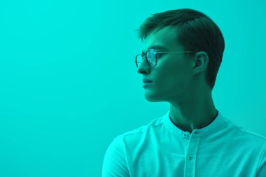 Zarif beyaz gömlekli ve şık gözlüklü yakışıklı sarışın bir adamın portresi. Başarılı bir insan. İş adamı. Turkuaz bir arka planda karışık ışıkla stüdyo çekimi. Gözlük modası. Boşluğu kopyala.