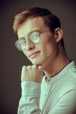 Zarif beyaz gömlekli, şık gözlüklü, kameraya bakıp gülümseyen sarışın bir adamın portresi. Gözlük modası. Başarılı bir insan. İş adamı. Gri bir arkaplanda stüdyo çekimi.