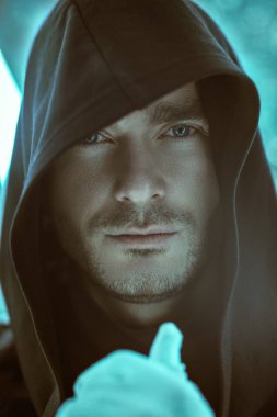 Fantezi kahramanı. Siyah bir bornoz giymiş, kafasında bir başlıkla neon lambaların ışığında duran cesur görünümlü yakışıklı bir adamın yakın çekimi. Uzay hakkında bilim kurgu. Sanal tema.