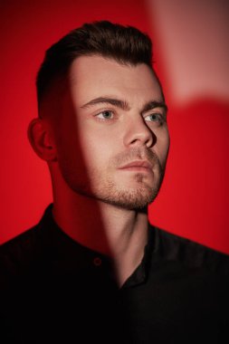 Kırmızı arka planda duran ve düşünceli görünen bir adamın portresi. Psikolojik sanat portresi.