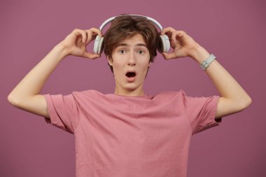 Şaşırmış bir genç çocuk kulaklıkla müzik dinler. Tozlu bir gül arka planına karşı stüdyo portresi. 
