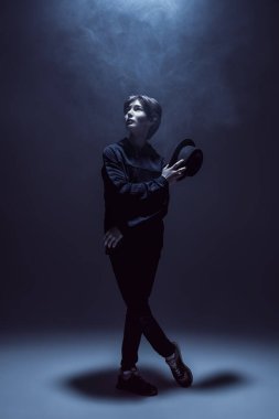 Stüdyoda koyu gri bir arka planda koyu mavi ışık altında şapkalı şık bir gencin portresi. Resim..