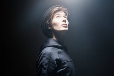 Stüdyoda koyu gri arka planda şapka takan şık genç bir çocuğun stüdyo portresi. Gençler için sıradan bir tarz. Duygular.