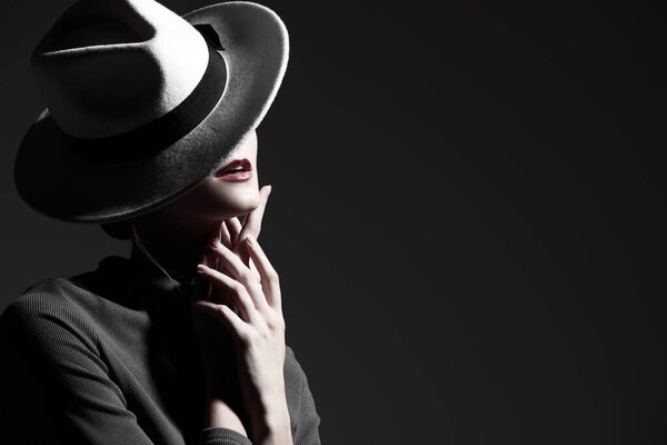 Fashion portrait of a beautiful lady in a white felt hat covering her face. Black studio background with copy space. Feminine beauty and elegant style. 