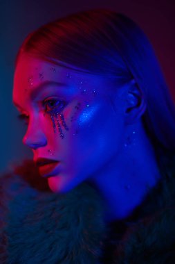 Sanatsal sim makyajı. Güzellik, kozmetik. Göz kamaştırıcı bir modern kızın portresi. Parlak makyajı, parlak gözyaşları ve parlak mavi bir ışıkla yüzünde pullar. Gece kulübü. Moda makyaj. 