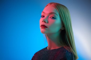 Güzellik konsepti, makyaj ve makyaj malzemeleri. Parlak makyajlı, mavi stüdyo arka planında düz sarı saçlı güzel bir manken kızı portresi. Uzayı kopyala Göz kamaştırıcı bir stil..