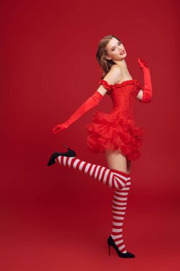 Kırmızı korse giyen, tüylü etek giyen ve yüksek topuklularla dans eden çekici, zeki bir kız. Kırmızı arka plan şenliği. Noel ve Yeni Yıl. 