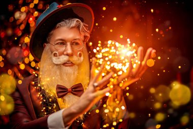 Yakışıklı, modern bir Noel Baba portresi zarif sakallı ve bıyıklı, şapka takan şık bir takım elbiseli ve altın ışıklarla çevrili gözlüklü. Sihirli Noel ve yeni yıl. Moda.. 