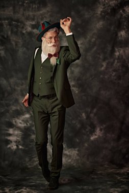 Zarif, beyaz sakallı ve bıyıklı, üç parçalı bir şenlik elbisesi ve klasik bir arka planda şapkası olan yakışıklı bir Noel Baba 'nın tam boy fotoğrafı. Moda ve Noel, Yeni Yıl.