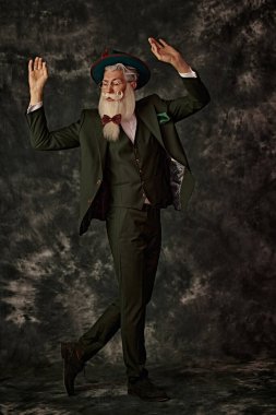 Yakışıklı bir Noel Baba 'nın uzun boylu portresi zarif beyaz sakallı ve bıyıklı üç parçalı şenlikli bir takım elbise ve klasik bir arka planda bir şapka. Moda ve Noel, Yeni Yıl.