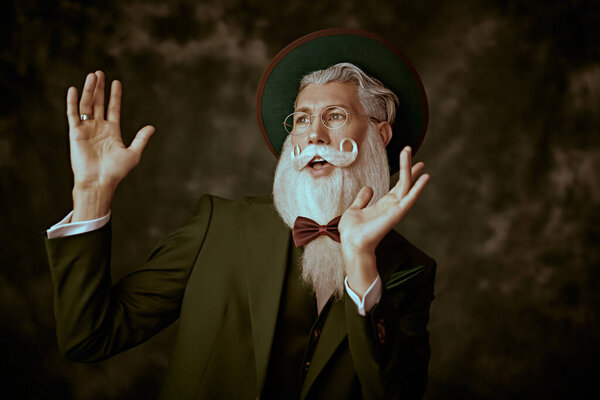 Portrait of a handsome Santa Claus with an elegant white beard and mustache in a festive green three-piece suit, a hat and spectacles on a vintage background. Fashion and Christmas, New Year.