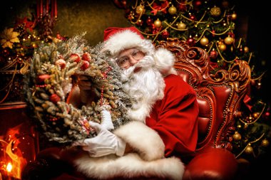 Nazik Noel Baba elinde Noel çelengiyle güzel bir Noel ortamında bir sandalyede oturuyor. Mutlu Noeller ve mutlu yıllar.!