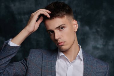 Klasik bir takım elbise ve koyu bir arka planda beyaz gömlek giyen zarif giyimli bir gencin portresi. Erkek modası. İş biçimi.