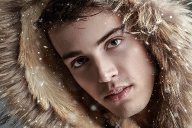 Kürk kapüşonlu kışlık ceketli yakışıklı bir esmer adamın yakın plan portresi. Erkekler kış modası. 