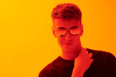 Siyah günlük kıyafetler ve güneş gözlüğü takmış, parlak sarı arka planda fotokopi alanı olan şık yakışıklı bir adam. Erkek modası ve tarzı.