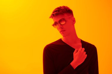 Siyah günlük kıyafetler ve güneş gözlüğü takmış, parlak sarı arka planda fotokopi alanı olan şık yakışıklı bir adam. Erkek modası ve tarzı.