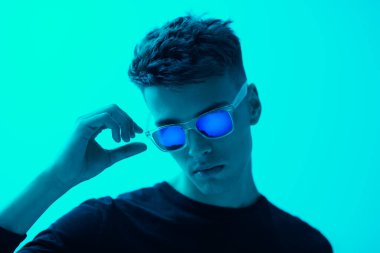 Siyah günlük kıyafetler ve parlak mavi bir arka planda poz veren gözlüklü bir adam. Erkek modası ve tarzı. Boşluğu kopyala.