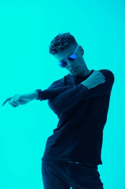 Siyah günlük giysiler içinde yakışıklı bir genç adam portresi ve parlak bir suda poz veren moda güneş gözlükleri. Erkek modası ve tarzı.