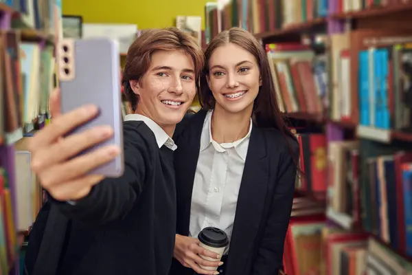 Happy modern students in black and white uniform taking a selfie in a library. Modern generation. Education.