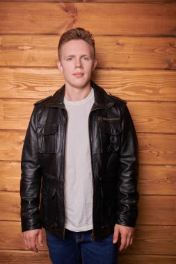 Ahşap bir duvarın yanında duran şık deri ceketli sarışın genç bir adamın portresi. Erkek modası, deri tarzı..