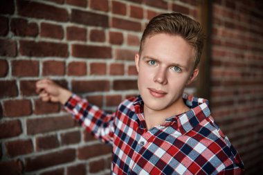 Gençler, yaşam tarzı. Kareli gömlekli yakışıklı modern bir adam tavan arası bir odada tuğla bir duvarın yanında duruyor. Sıradan erkek modası.. 