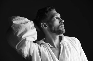 Siyah beyaz, beyaz, siyah arka planda geniş kollu, beyaz tişörtlü, olgun bir adamın resmi. 19. yüzyılın sonlarından 20. yüzyılın başlarına kadar yaşamış bir adamın tarihi portresi. Erkek güzeli.. 