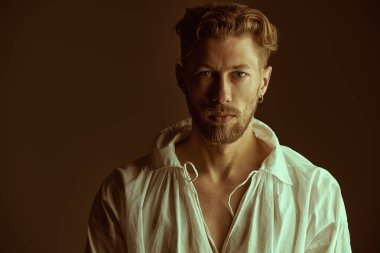 Beyaz tişörtlü, kızıl saçlı, yakışıklı olgun bir adam, şarap rengi bir arka planda poz veriyor. 19. yüzyılın sonlarından 20. yüzyılın başlarına kadar yaşamış bir adamın tarihi portresi. Erkek güzeli.. 